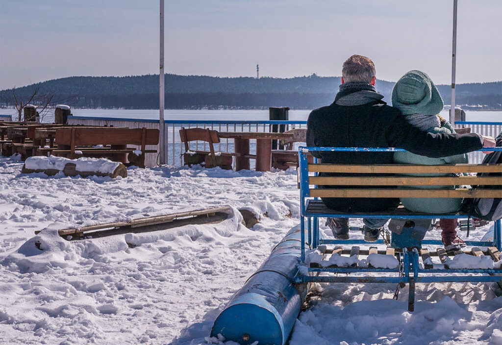 Zwei Menschen sitzen umarmt in einem Tretboot, das im Schnee auf einer Terrasse liegt.