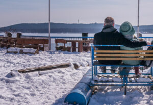 Zwei Menschen sitzen umarmt in einem Tretboot, das im Schnee auf einer Terrasse liegt.