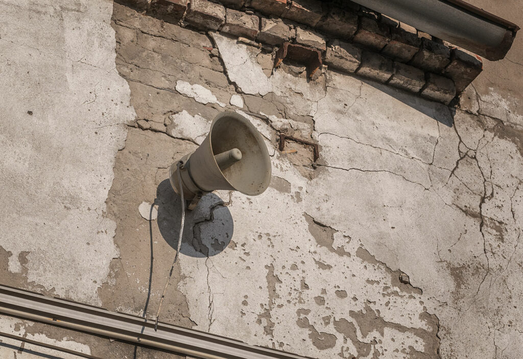 Ein Lautsprecher wie eine Flüstertüte hängt an einer maroden Wand