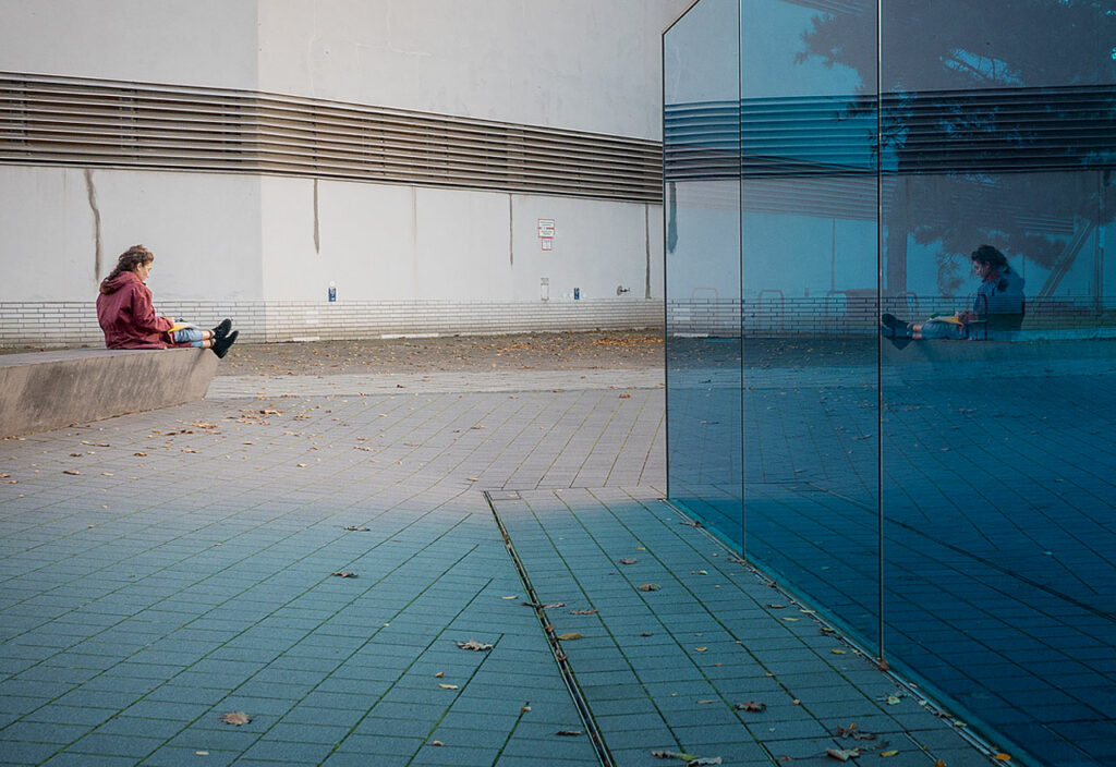 Ein Frau liest und spiegelt sich in der blauen Wand des Mahnmals T4